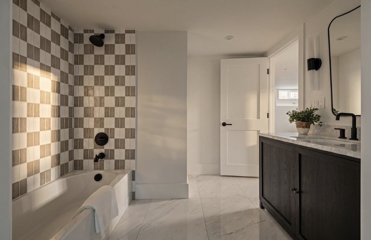 Bathroom with a checkerboard tile tub surround, dark wood vanity, black fixtures and marble floors