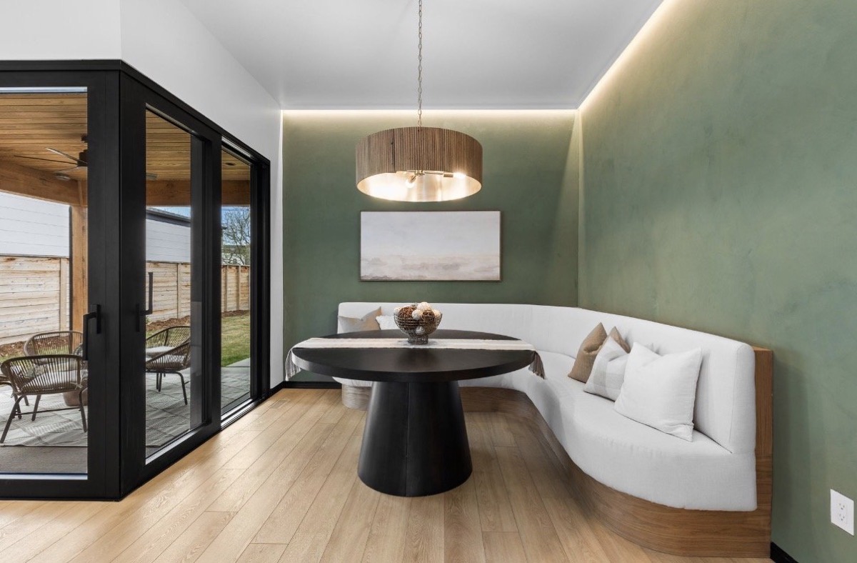 Breakfast nook with a curved white banquette, round black pedestal table and green plaster walls