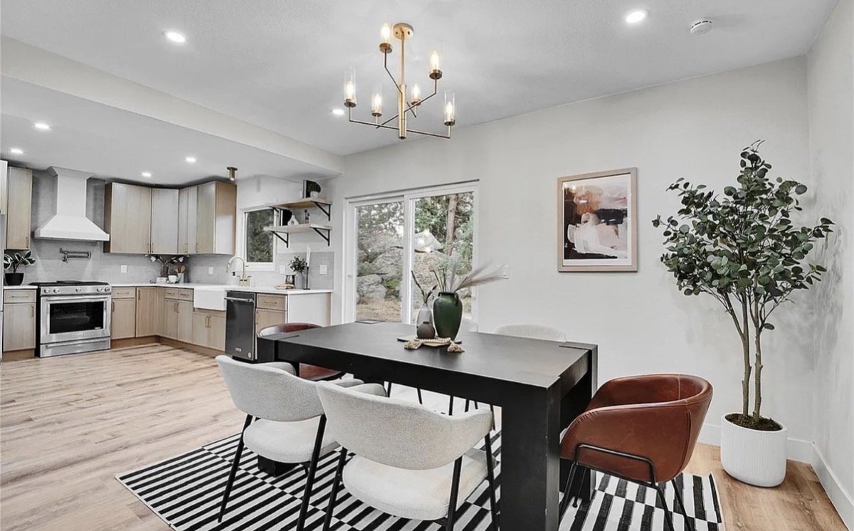 Dining room with a black table, white and cognac chairs, striped rug and brass chandelier