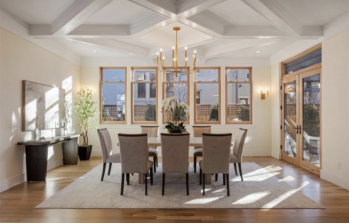 Dining room with a coffered ceiling, brass chandelier and gray upholstered dining chairs