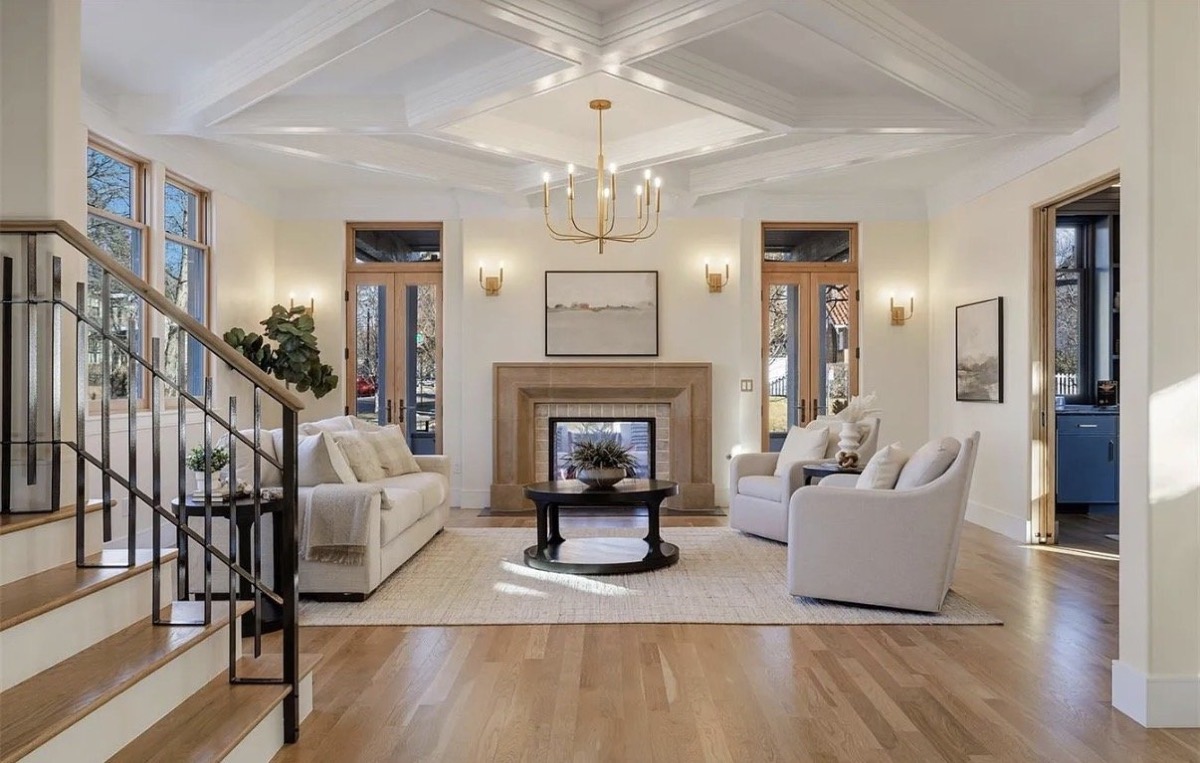 Formal living room with a coffered ceiling, limestone fireplace, brass chandelier and pair of white swivel chairs