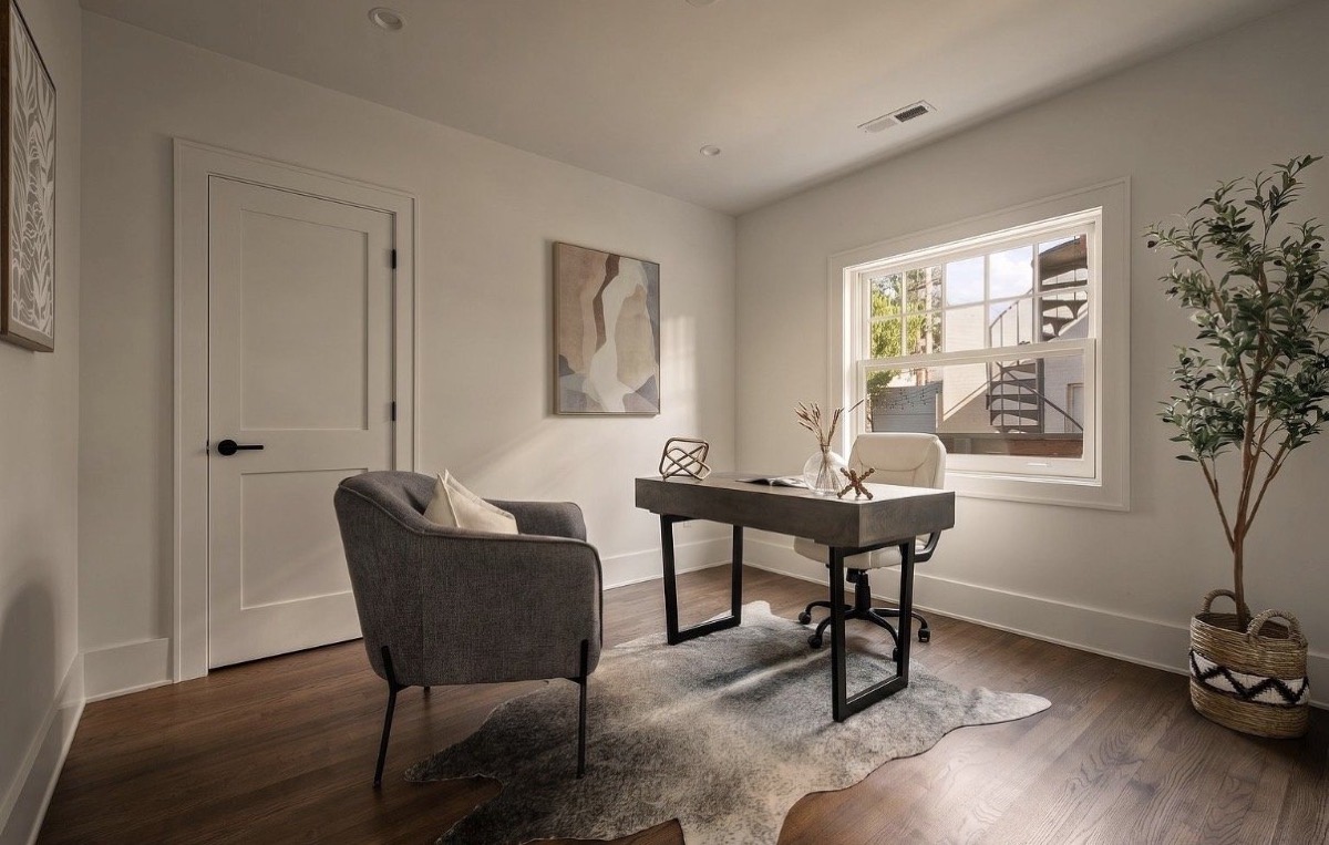 Home office with a black writing desk, gray accent chair, cowhide rug and abstract art on dark wood floors