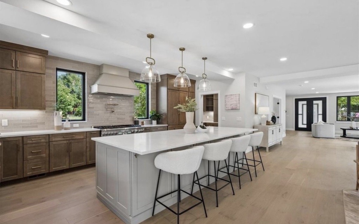 Kitchen with a white island, glass globe pendants, white counter stools and dark wood cabinetry