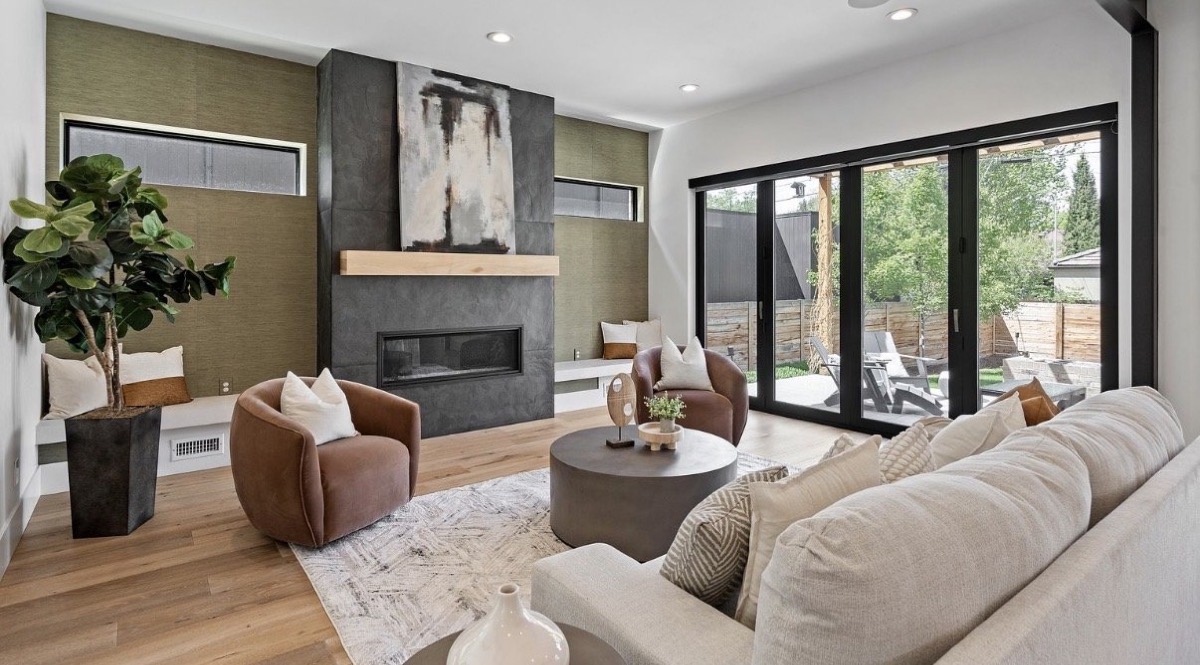 Contemporary living room with a dark tile fireplace, cognac accent chairs, cream sectional and folding glass patio doors