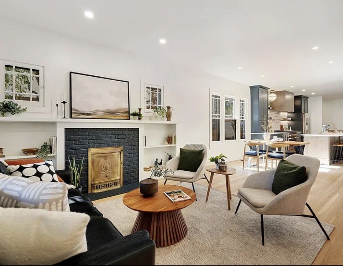 Living room with a navy painted brick fireplace, brass screen, olive green pillows and a round wood coffee table