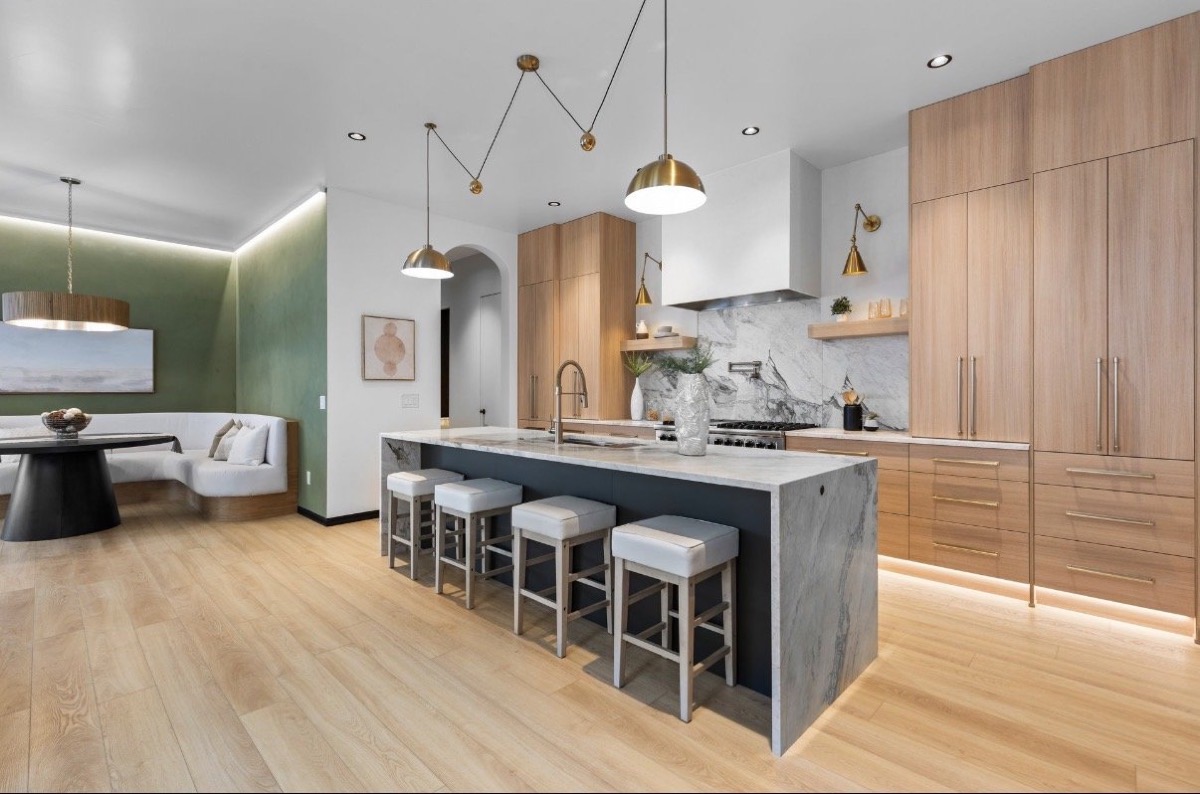 Modern kitchen with a waterfall island, brass pendants, flat-panel oak cabinets and a green dining banquette