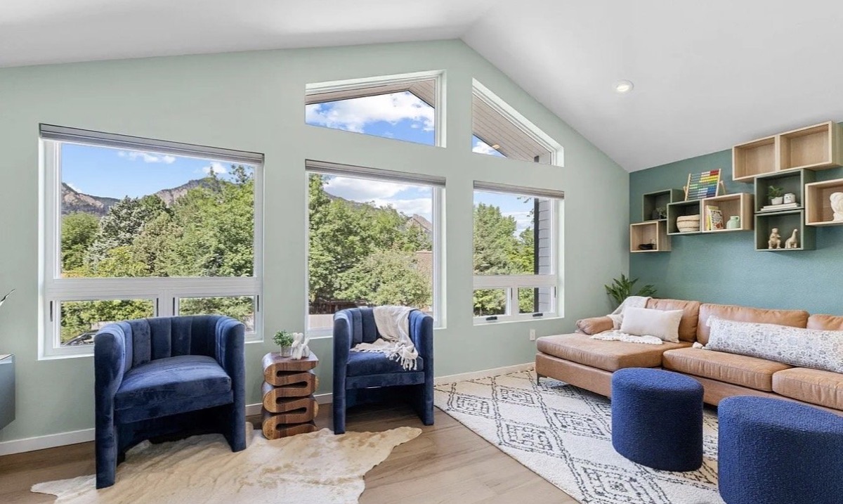 Vacation rental living room with mountain views, sage green walls, navy velvet chairs and a cognac sofa