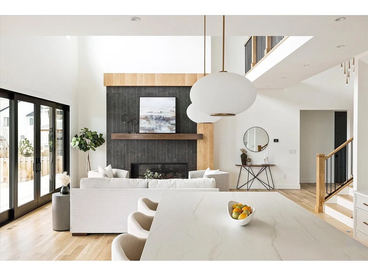 Open-concept great room with a dark brick fireplace, white oak mantel, marble island and oversized globe pendants
