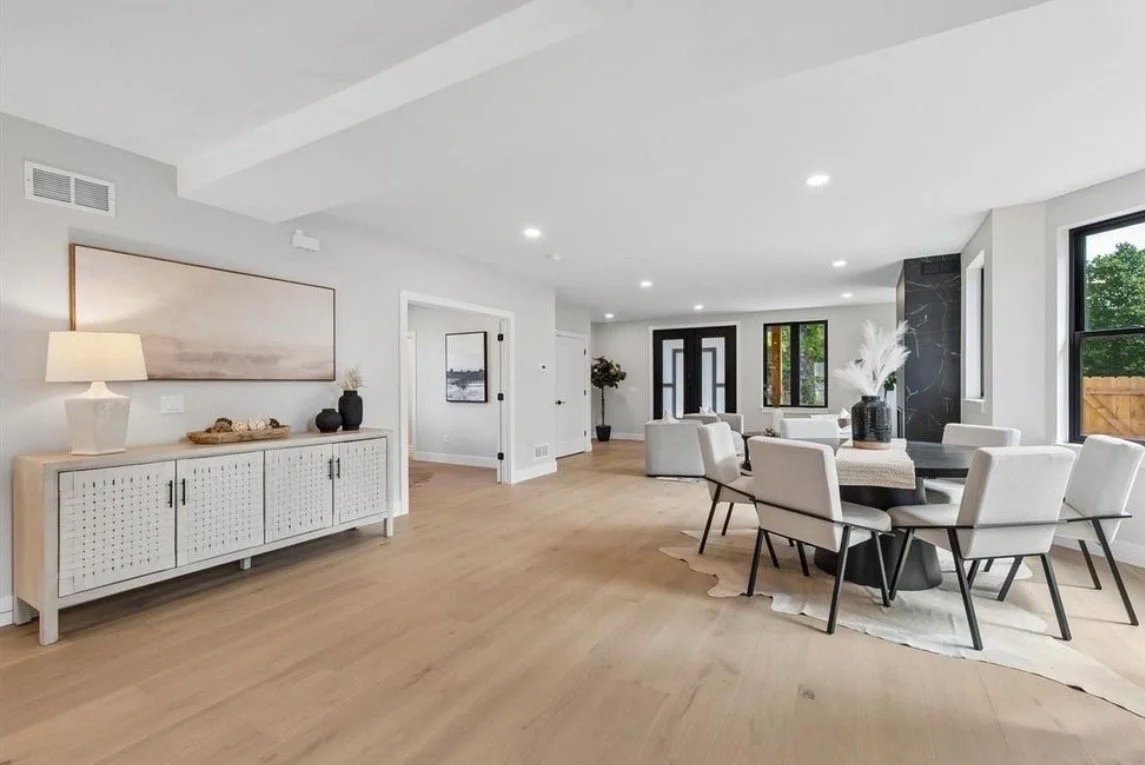 Open living and dining space with white oak floors, a cane-front sideboard and landscape art