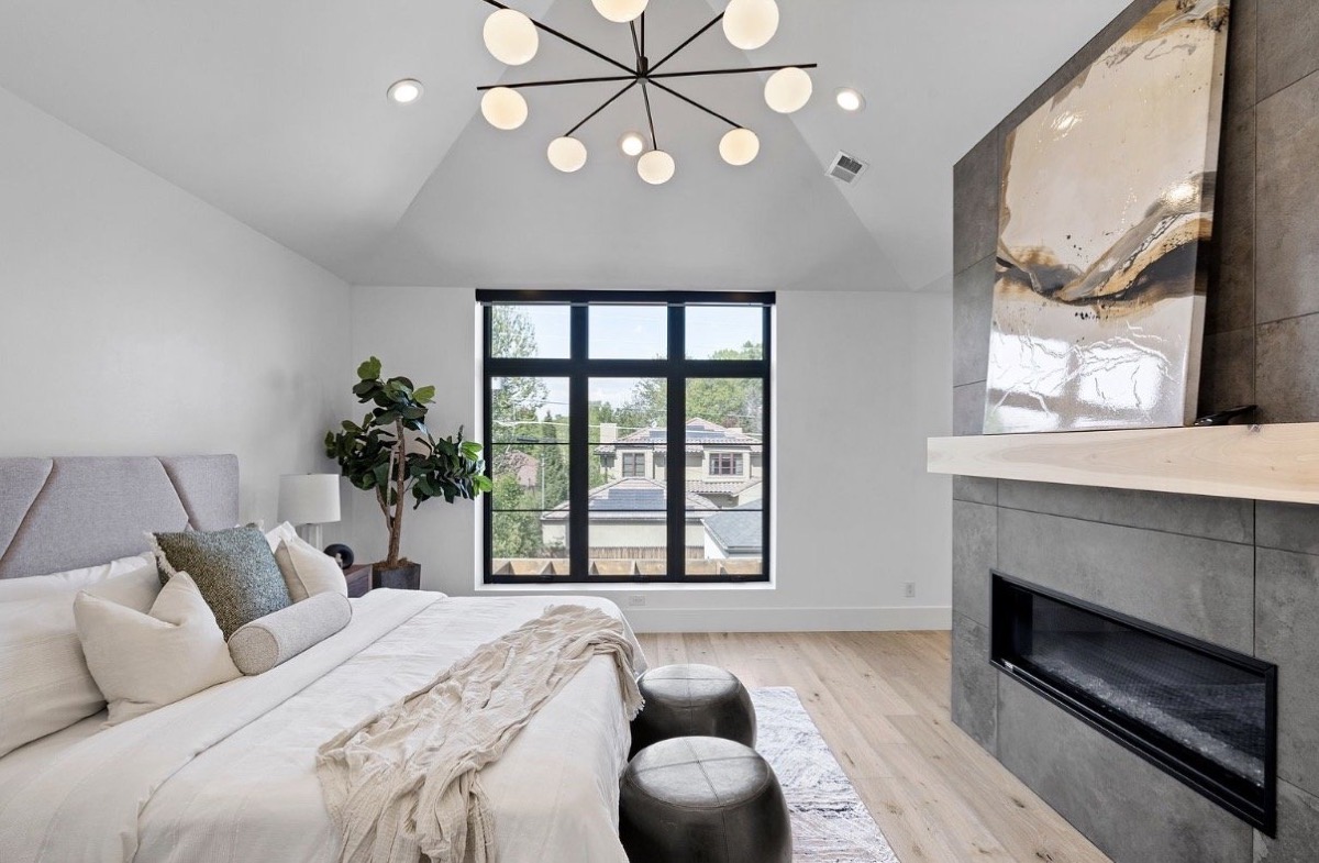 Primary bedroom with a sputnik chandelier, tiled linear fireplace, upholstered bed and leather ottomans