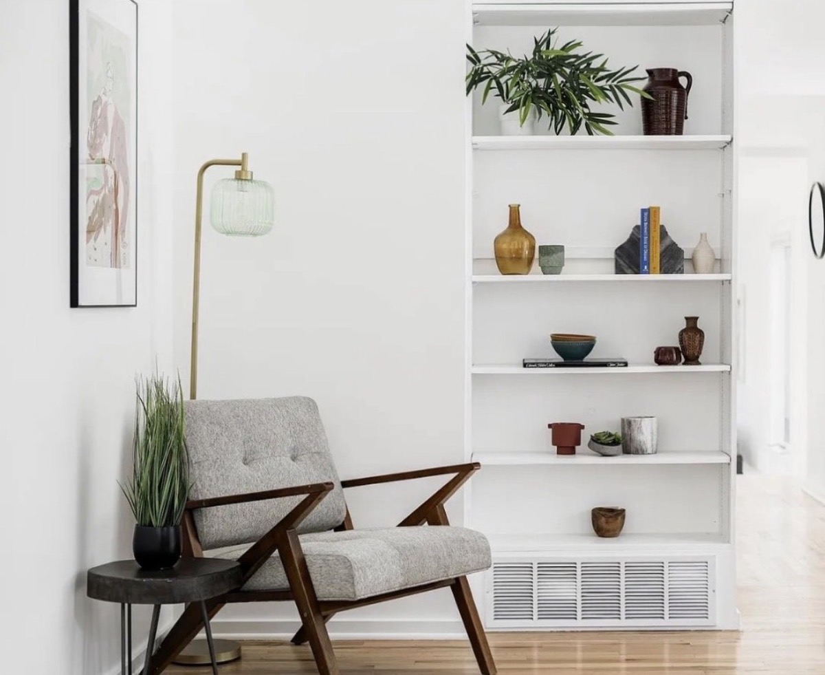Reading corner with a mid-century lounge chair, brass floor lamp and styled white shelves with ceramics