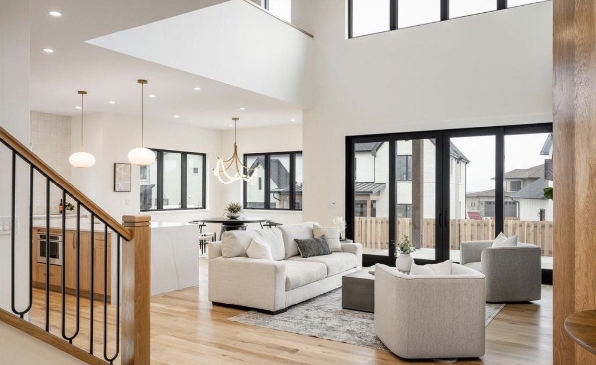 Two-story great room with white sofas, a tufted ottoman, glass pendants and black folding patio doors