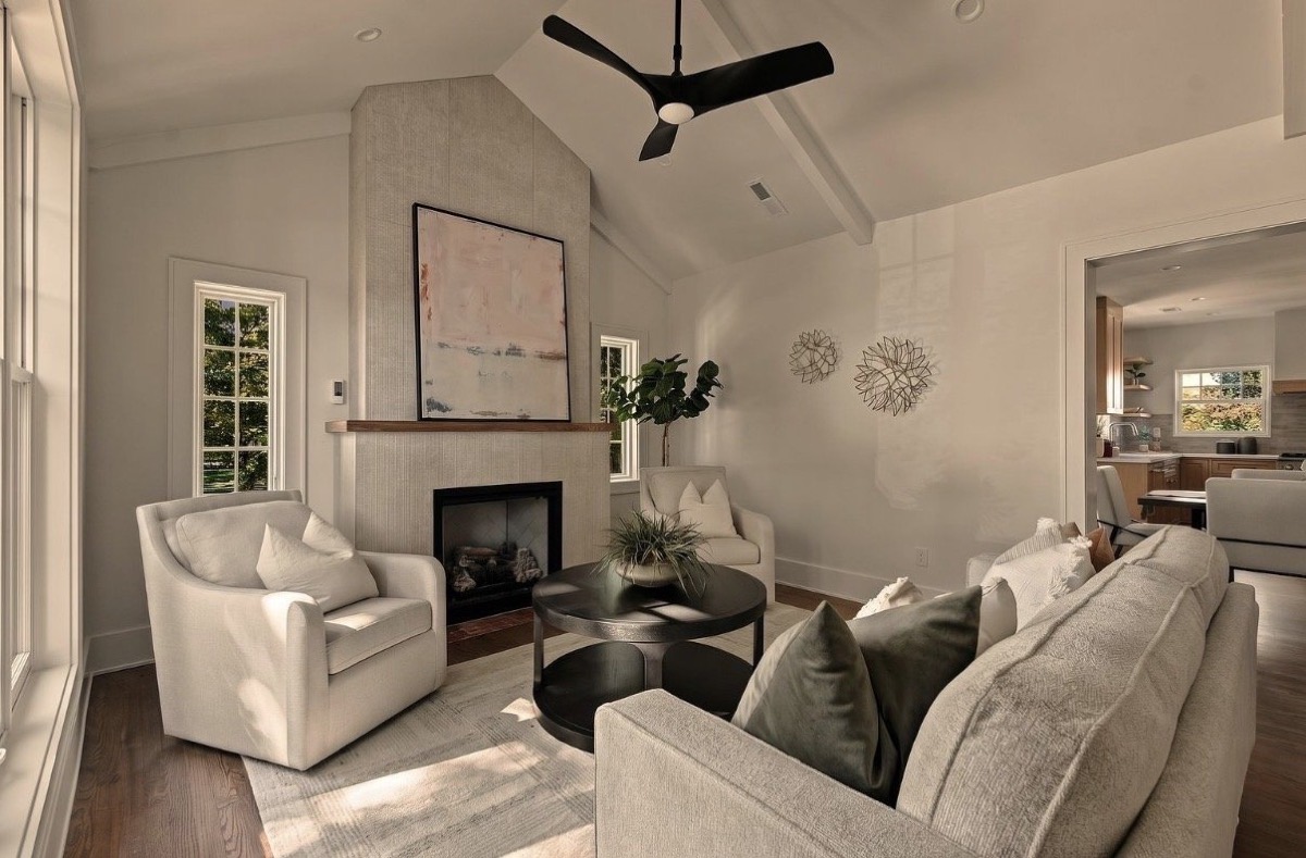 Vaulted living room with a cream plaster fireplace, black ceiling fan, upholstered swivel chair and large abstract painting
